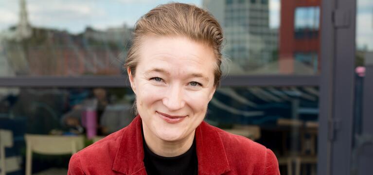 Photo of a woman with short hair a black shirt and a maroon jacket