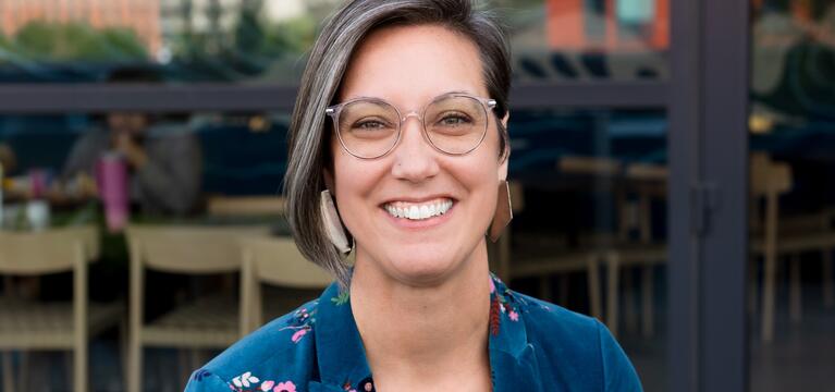 Photo of a woman with brown chin length hair glasses and a teal jacket