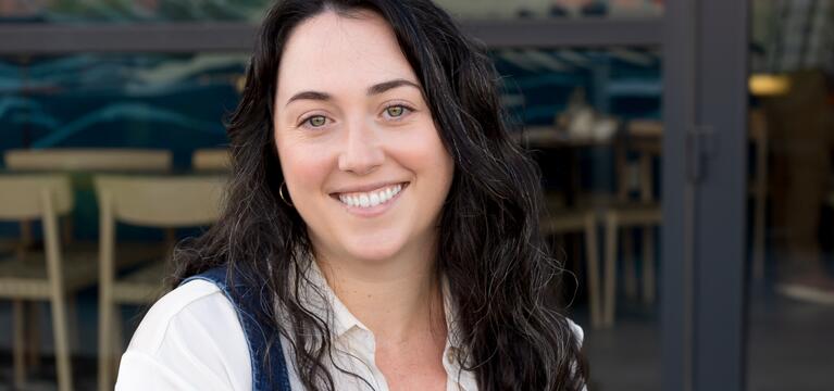 Photo of a woman with dark shoulder length hair a white shirt and a blue vest