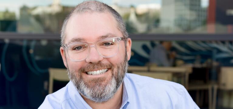 Photo of man with short hair gray beard and clear glasses in a blue shirt