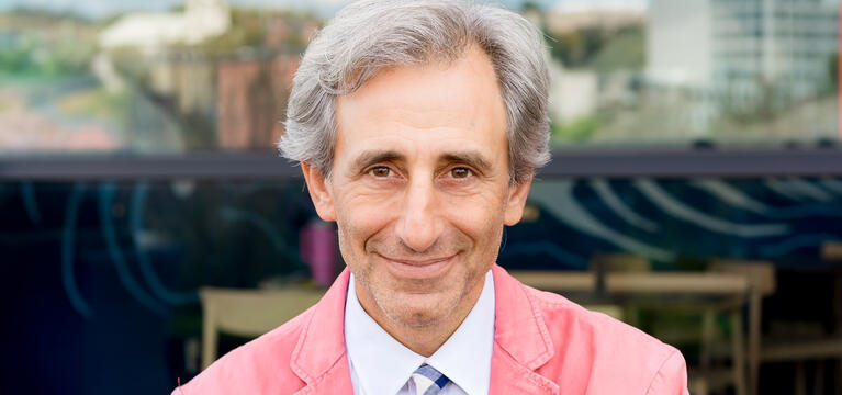 Photo of a man with gray hair a white shirt a pink jacket and a multicolored tie