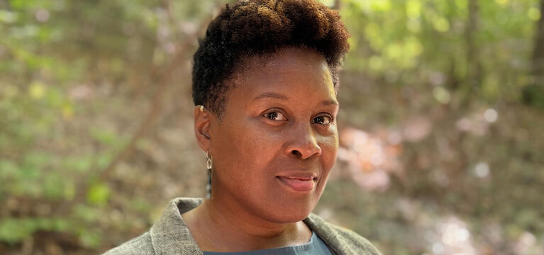 Photo of Shakiyla Smith-Sengu, a black woman with short hair in a teal shirt and gray coat