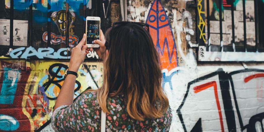 Image of a woman taking a photo on her phone of colorful graffiti, by Annie Spratt