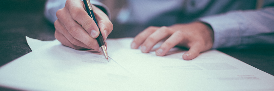 Photo of a white person in a blue business shirt writing on paper