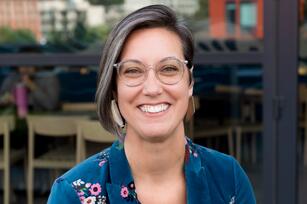Photo of a woman with brown chin length hair glasses and a teal jacket