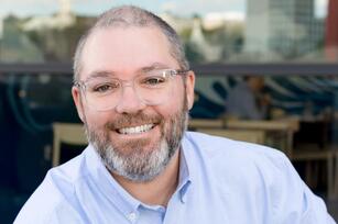 Photo of man with short hair gray beard and clear glasses in a blue shirt