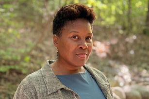 Photo of Shakiyla Smith-Sengu, a black woman with short hair in a teal shirt and gray coat