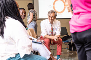 Photo of group of people focused on a man leaning forward in a chair smiling